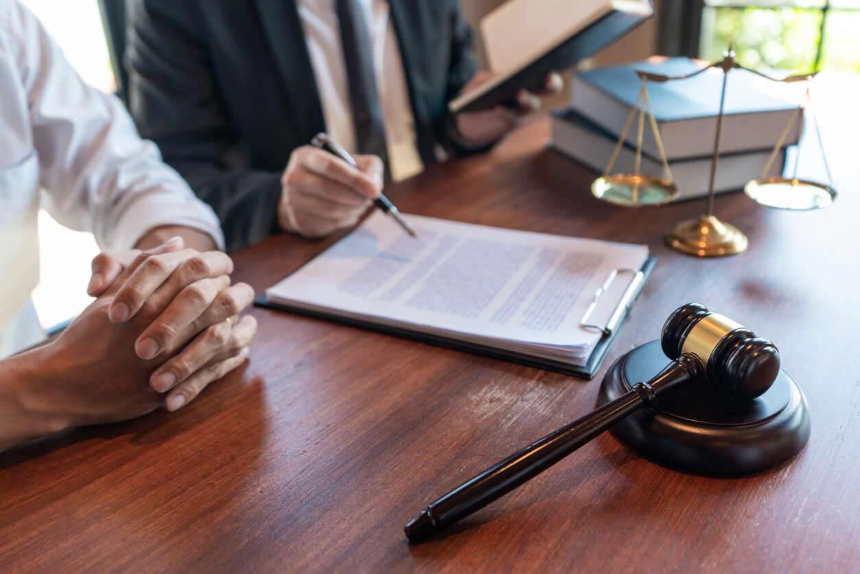 Pasadena Personal Injury Lawyer Personal injury lawyer and client discussing a injury claim form while sitting and gavel and scale of justice on the table.<br />