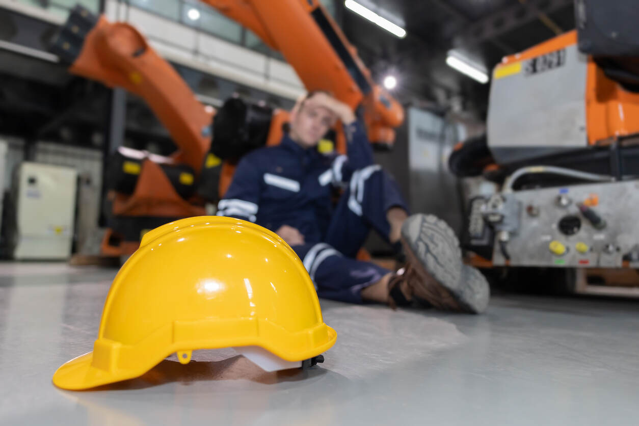 Glendale worker compensation lawyer Injured worker sitting on factory floor with hard hat in foreground, symbolizing workplace injury.