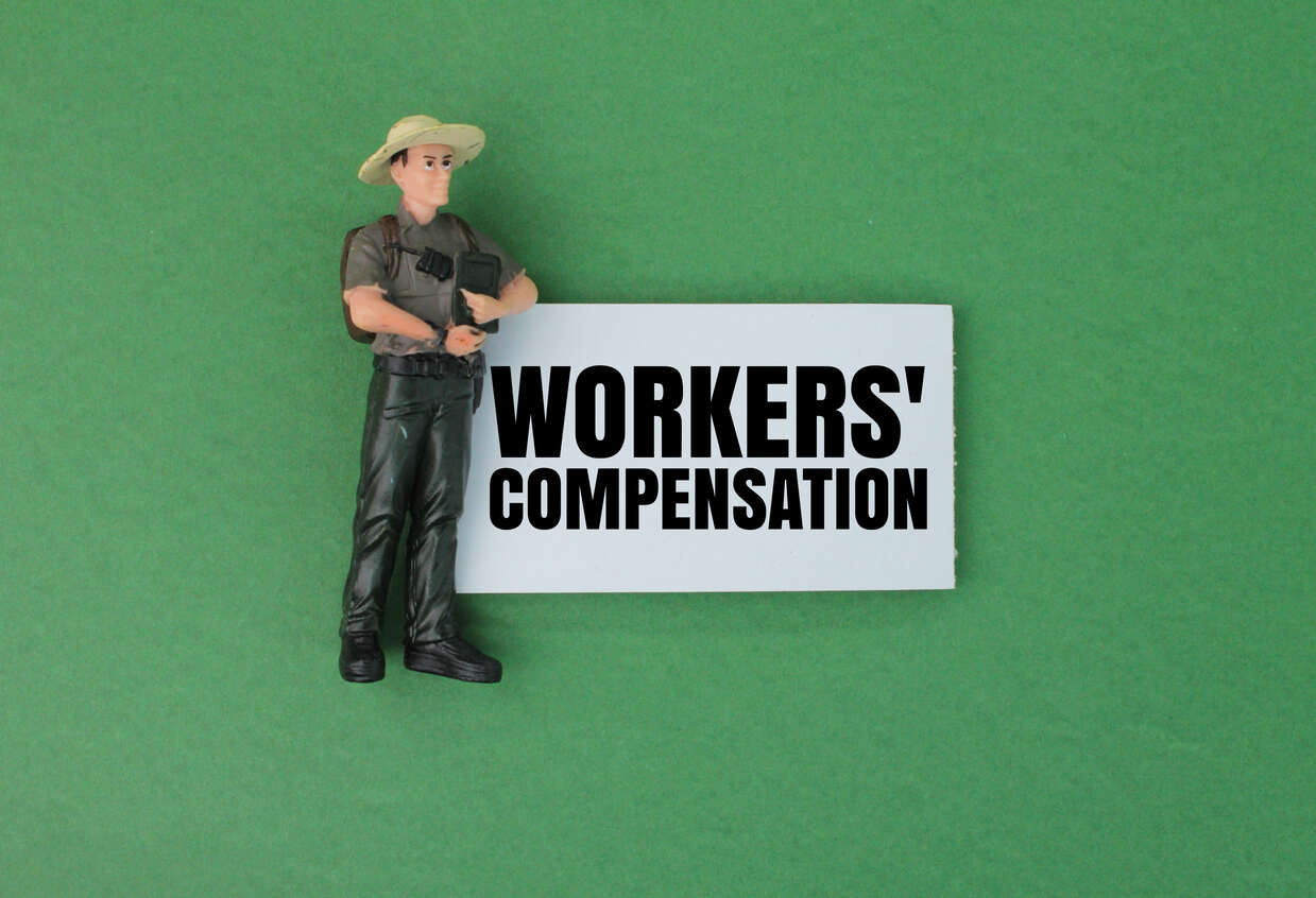 Long Beach Worker Compensation Lawyer Miniature construction worker next to a 'WORKERS' COMPENSATION' sign, symbolizing legal aid.