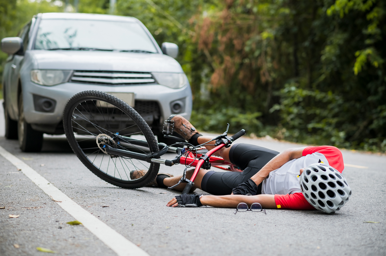 about-3 Ciclista tendido en la carretera junto a una bicicleta caída tras una colisión con un automóvil cercano.