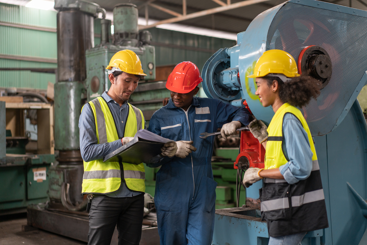 Industrial workers reviewing documents together on a factory floor, representing discussions about pay, job duties, and wage fairness