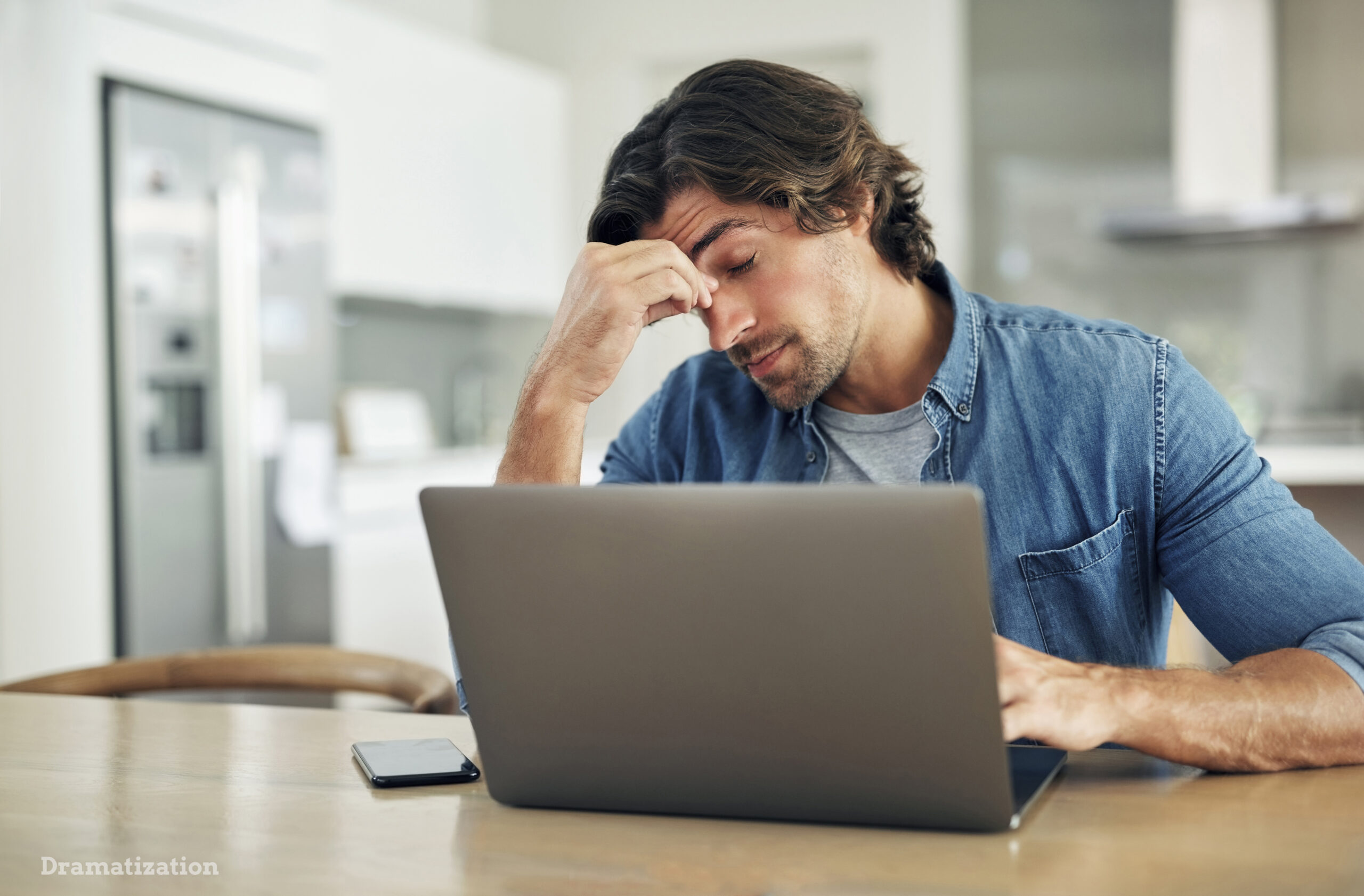 Former employee sitting at a table with a laptop, looking stressed and holding his forehead while reviewing information after being wrongfully terminated