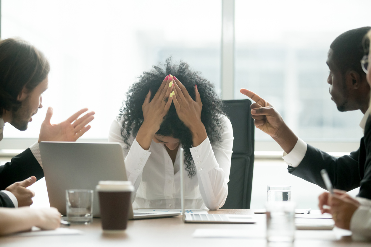 Gender Discrimination Attorney concept image showing a distressed employee covering her face while coworkers point and argue during a tense office meeting