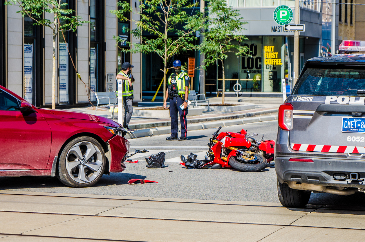 Police officers at the scene of a motorcycle accident injury, with a severely damaged red motorcycle and a car involved in the crash.