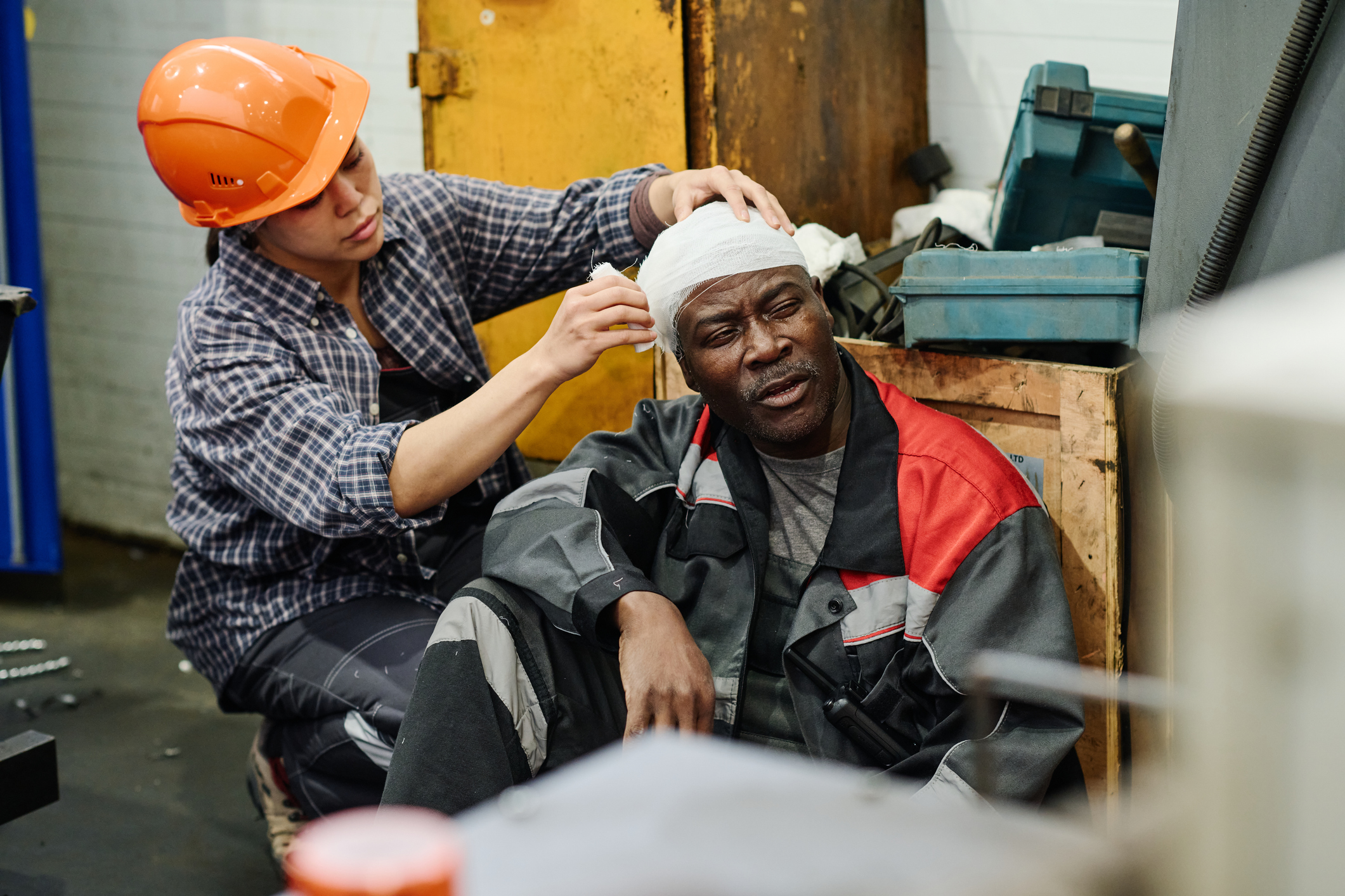 Assisting Injured Colleague in Industrial Setting Worker receiving first aid for a possible traumatic brain injury, with a colleague bandaging his head after a workplace accident.