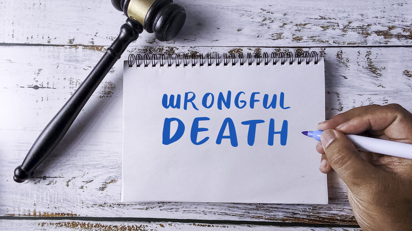 Legal concept image showing the words ‘Wrongful Death’ written on a notepad beside a judge’s gavel and a hand holding a pen.