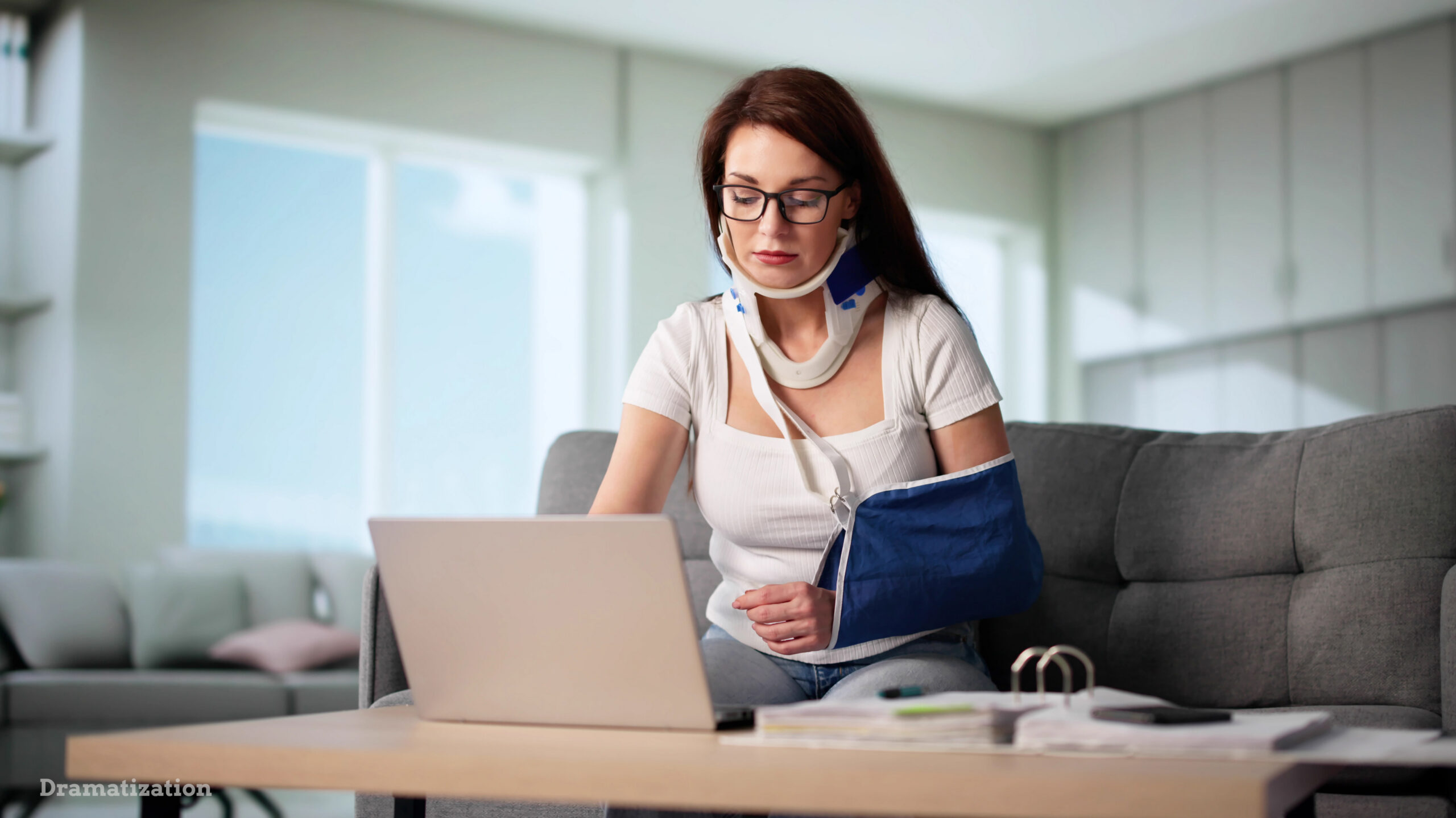 Injured worker wearing a neck brace and arm sling while using a laptop at home, reviewing documents related to workers’ compensation